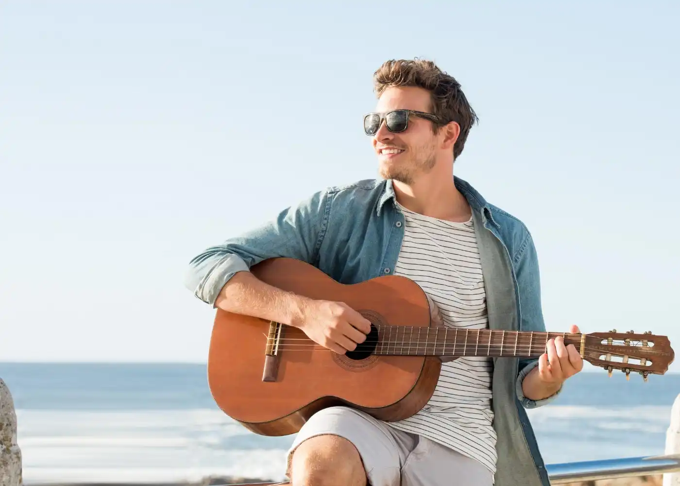 man playing his guitar near an ocean