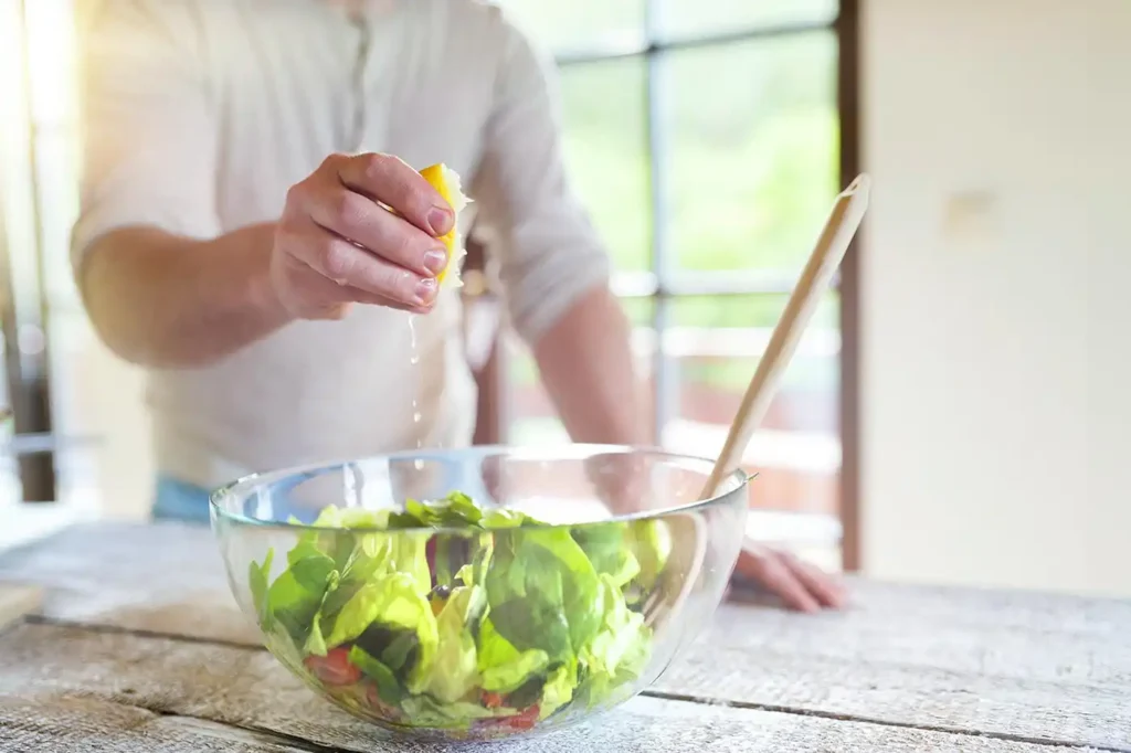 Man putting dressing on a green salad in a large bowl.