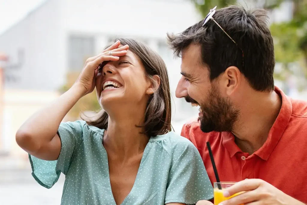 A man and woman share a joyful moment, laughing together on a bench, symbolizing hope in drug and alcohol recovery