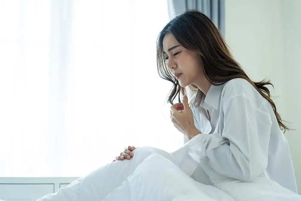 A woman sitting on a bed with hands on her chest, distress due to chronic breathing problems