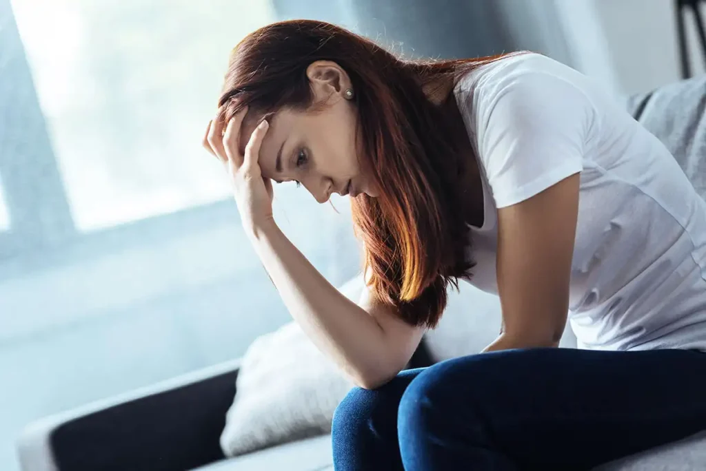 A woman sits on a couch, her head in her hands, reflecting on her journey through overcoming shame and guilt in addiction recovery