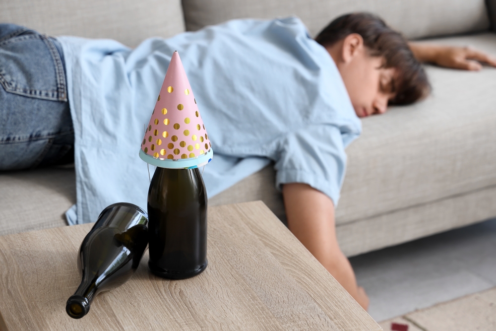 Male sleeping on the couch with alcohol bottles around him dealing with a hangover