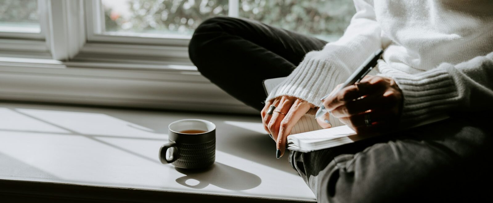 Person journaling on a window seat with a cup of coffee during alcohol addiction treatment in Menifee